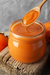 Photo of Spoon with delicious persimmon jam over jar, closeup