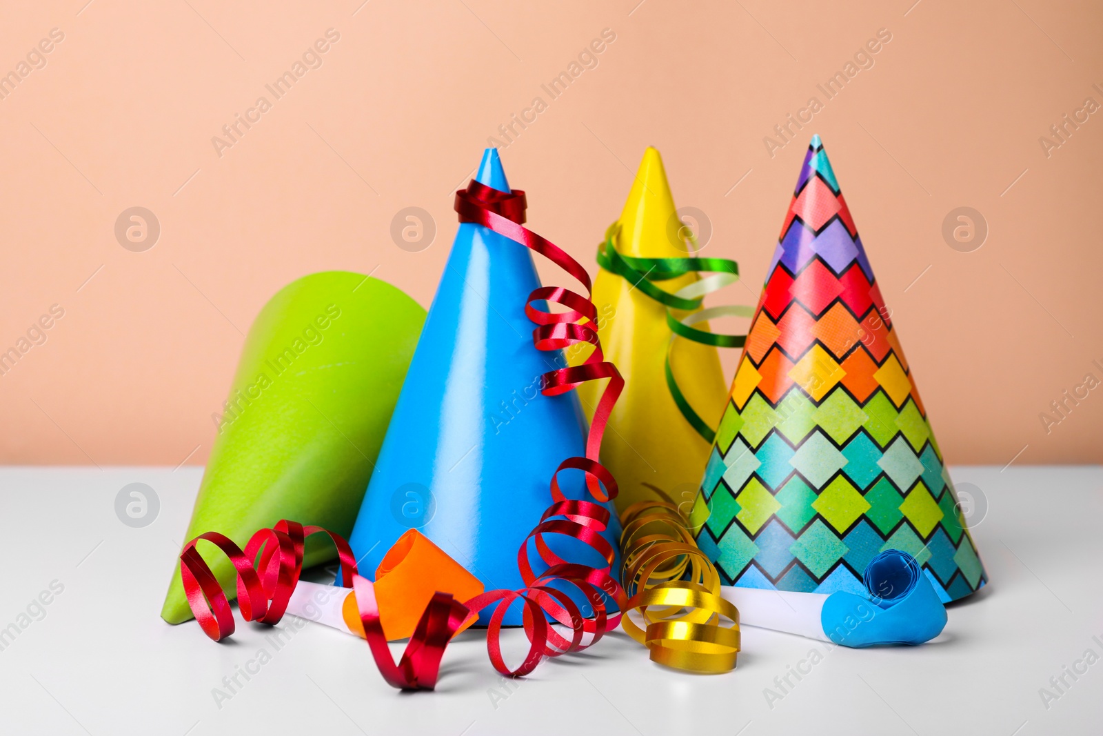 Photo of Colorful party hats, streamers and blowers on white table. Birthday celebration