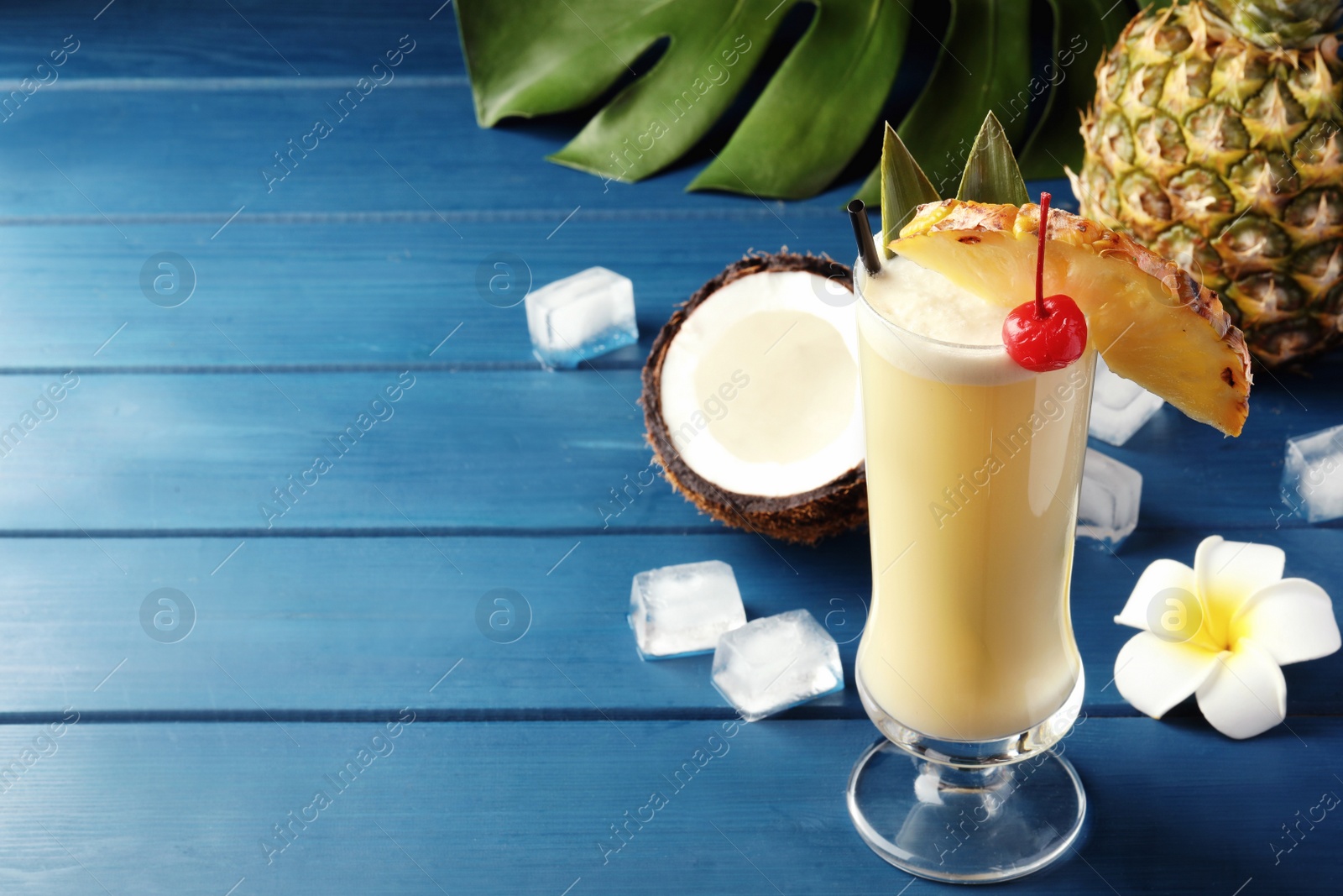 Photo of Tasty Pina Colada cocktail and ingredients on blue wooden table, space for text