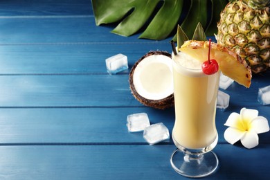 Tasty Pina Colada cocktail and ingredients on blue wooden table, space for text