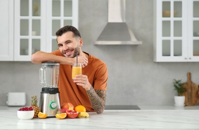 Handsome man with delicious smoothie at white marble table in kitchen. Space for text