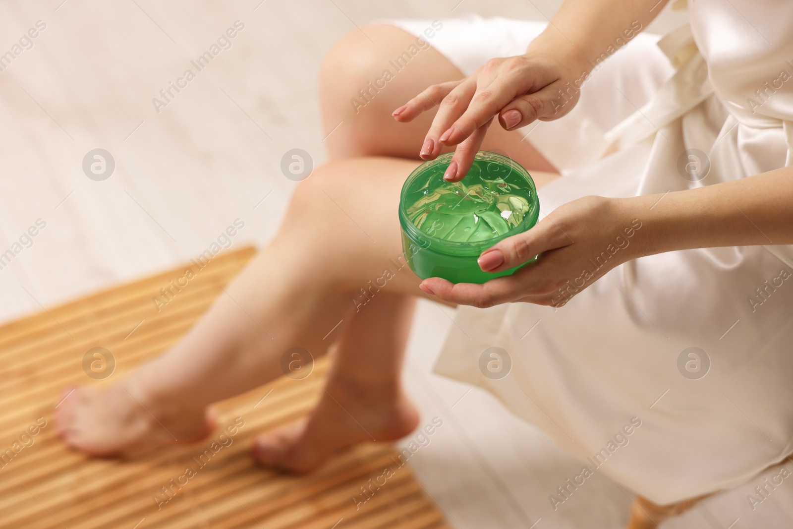 Photo of Young woman holding jar of aloe gel indoors, closeup