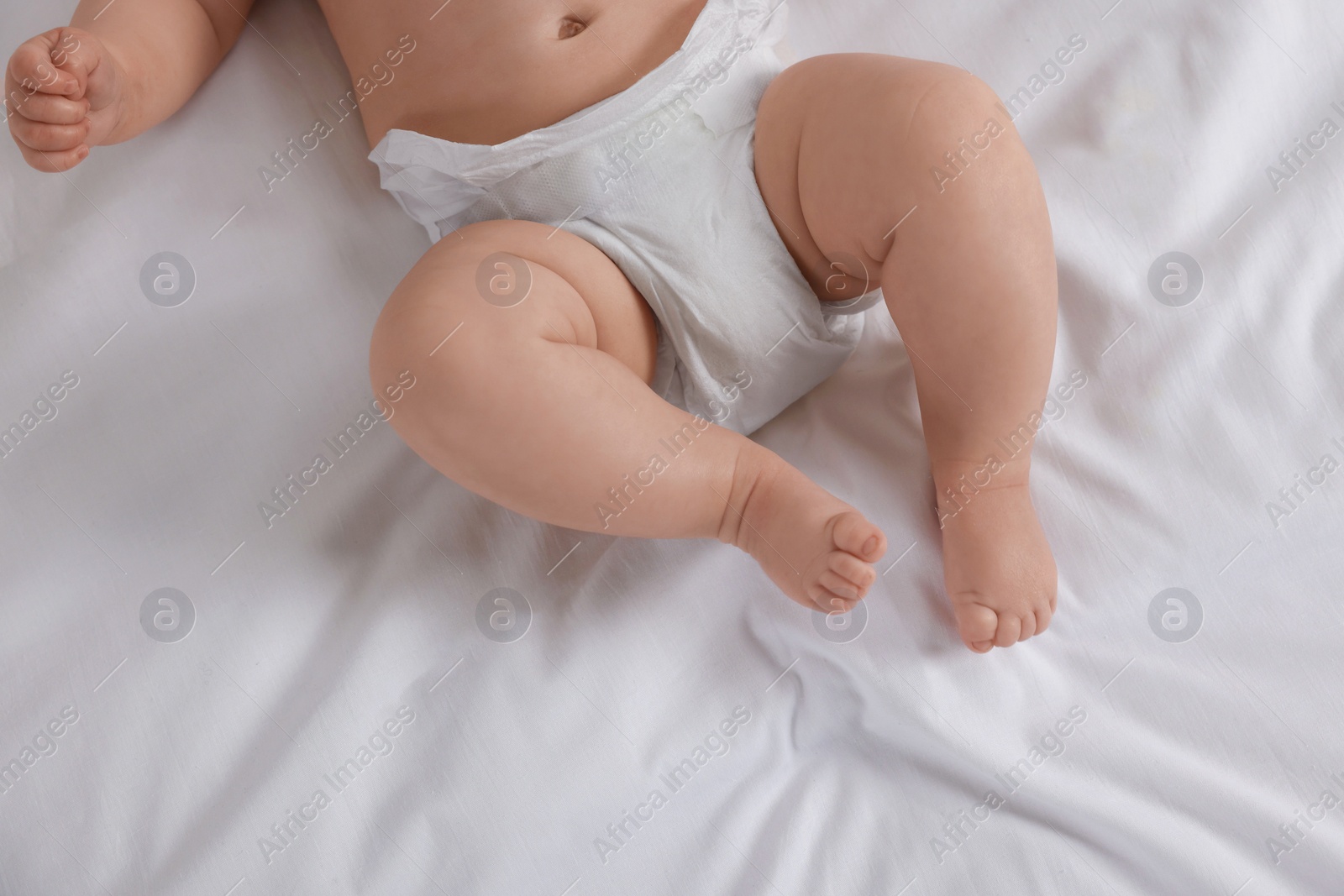 Photo of Little baby in diaper lying on bed, top view