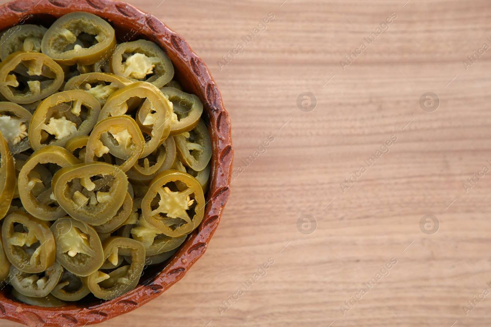 Photo of Pickled green jalapeno peppers on wooden table, top view. Space for text