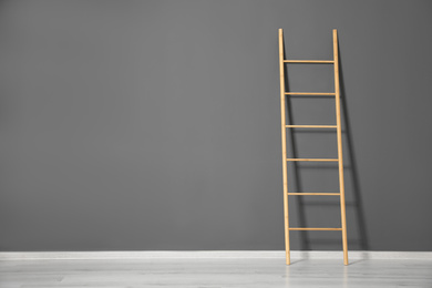 Photo of Modern wooden ladder near grey wall. Space for text