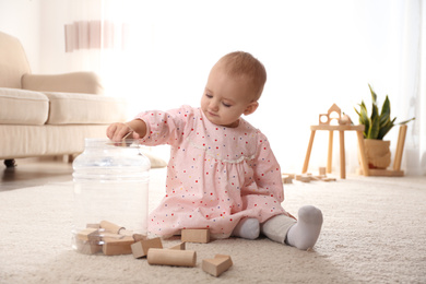 Cute child playing with wooden building blocks on floor at home