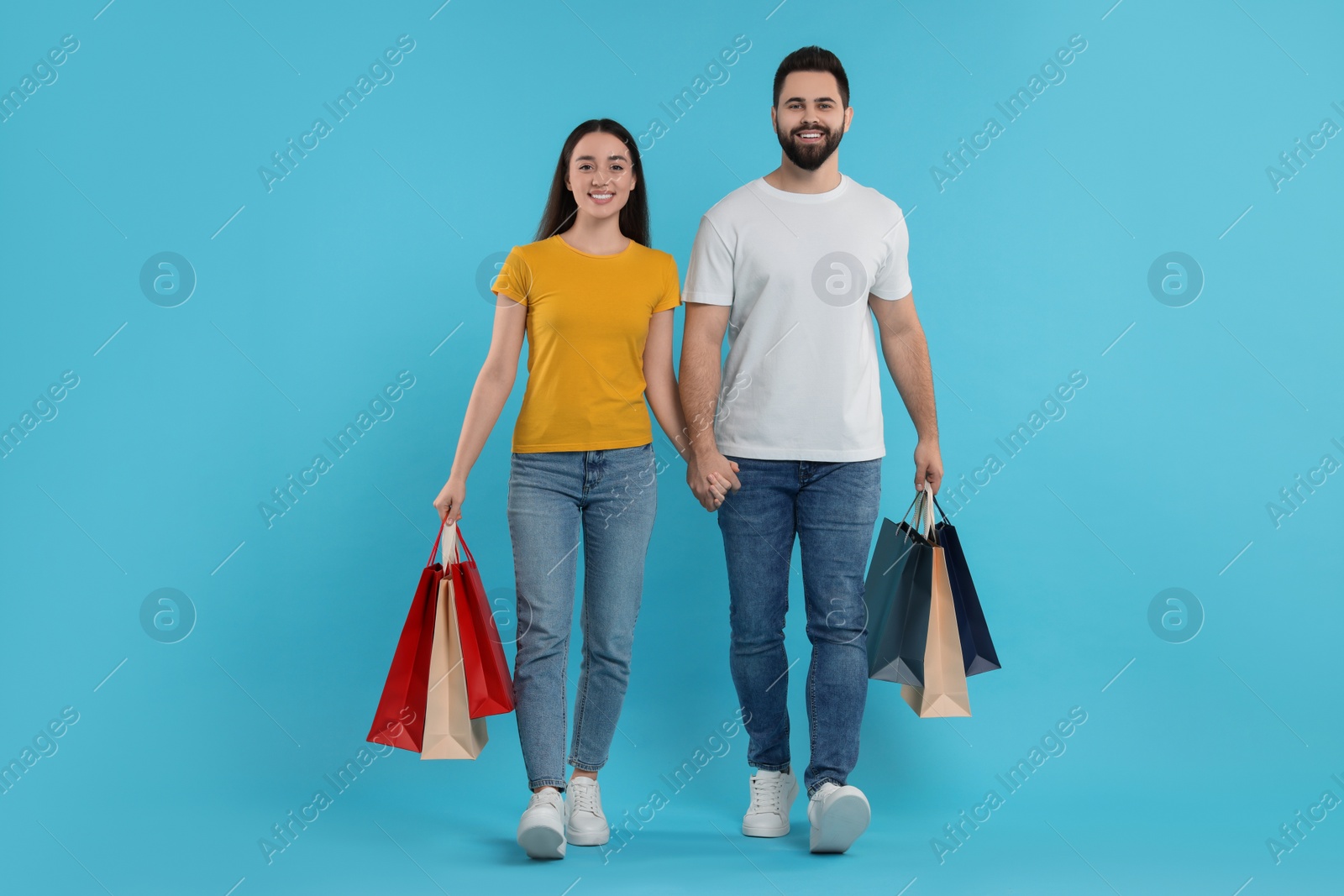 Photo of Happy couple with shopping bags on light blue background