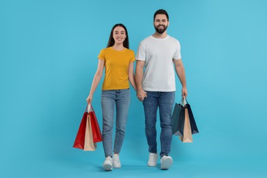 Photo of Happy couple with shopping bags on light blue background