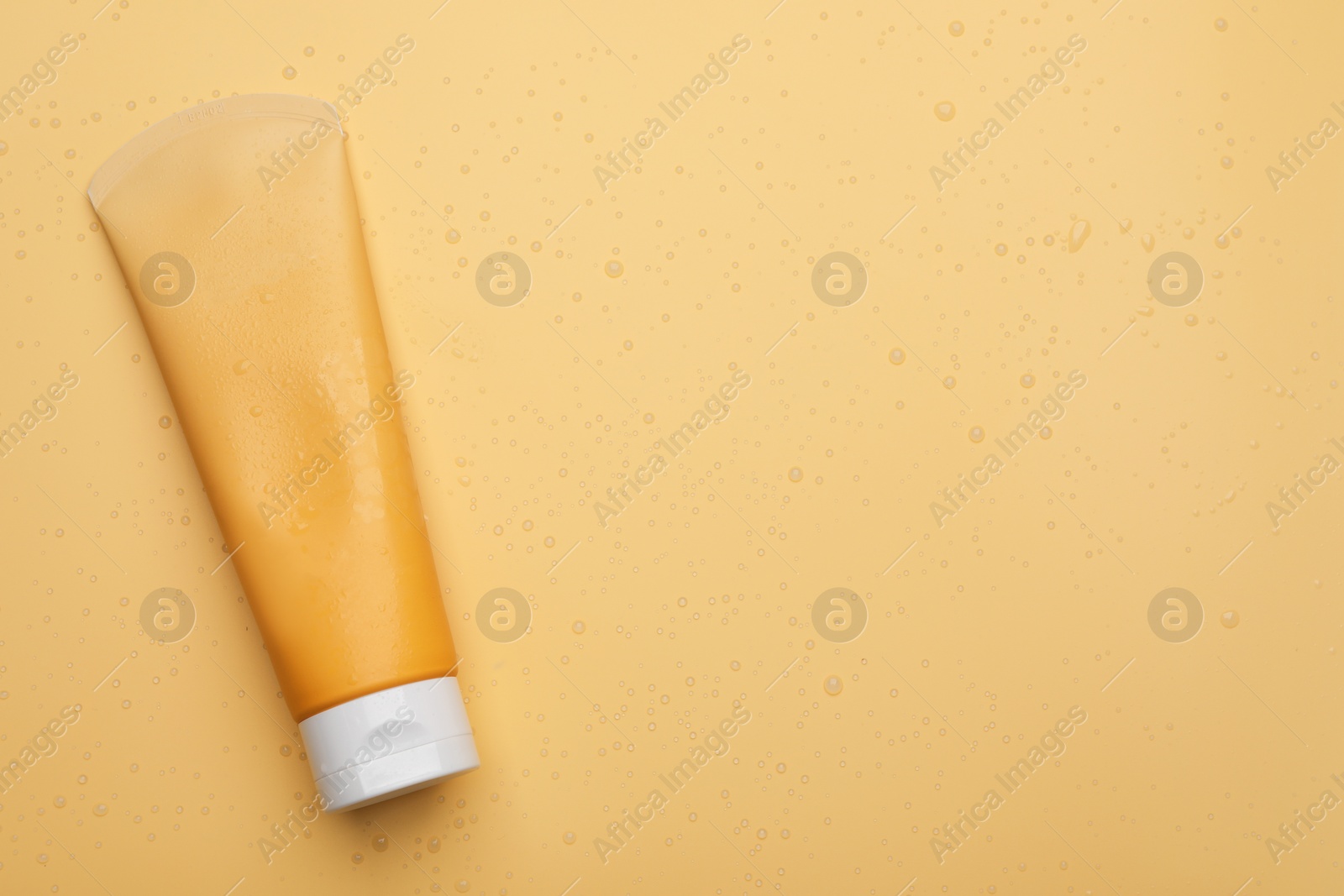 Photo of Wet tube of face cleansing product on pale orange background, top view. Space for text