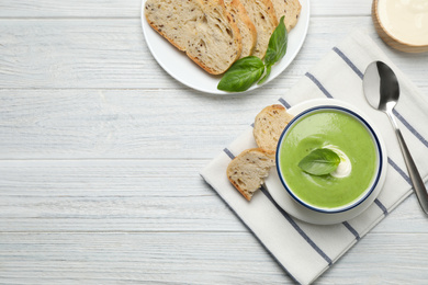 Photo of Tasty homemade zucchini cream soup served on white wooden table, flat lay. Space for text