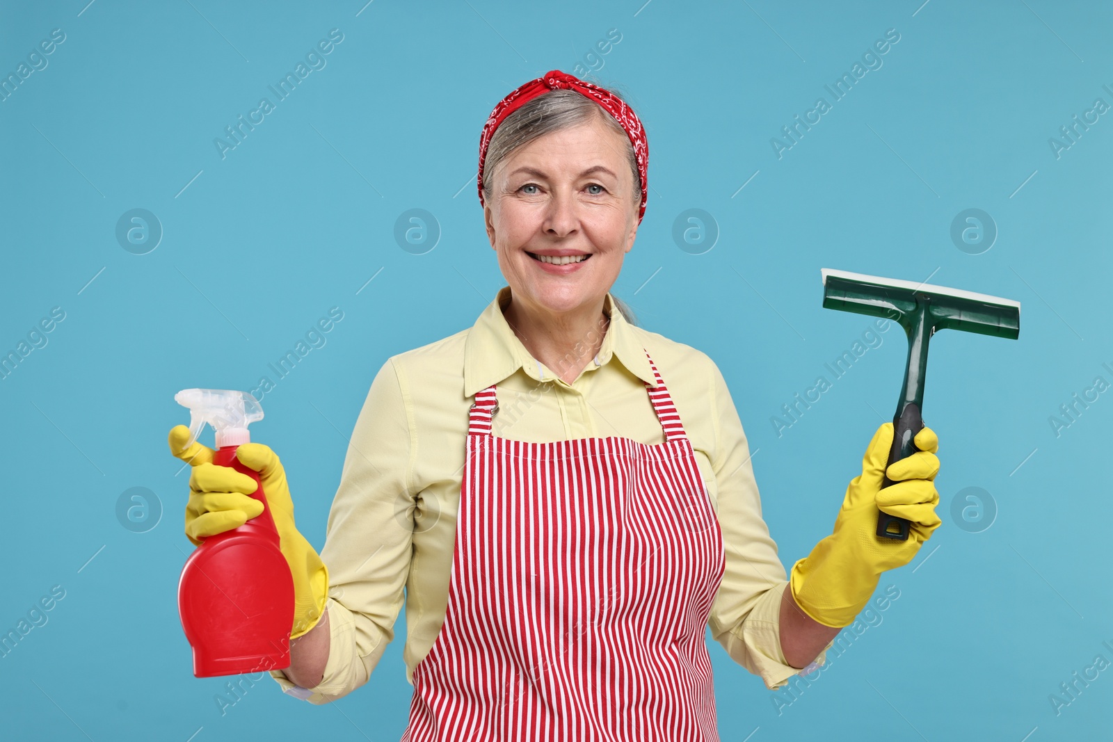Photo of Happy housewife with spray bottle and squeegee on light blue background