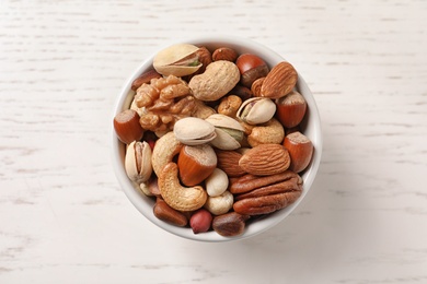 Bowl with organic mixed nuts on white wooden background, top view
