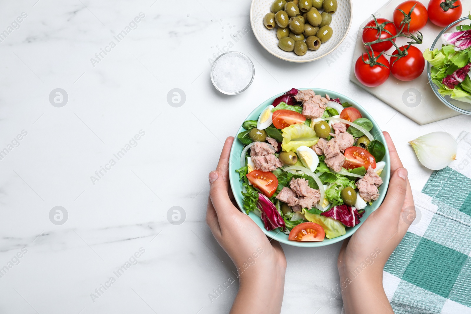 Photo of Woman holding bowl of delicious salad with canned tuna at white table, top view. Space for text