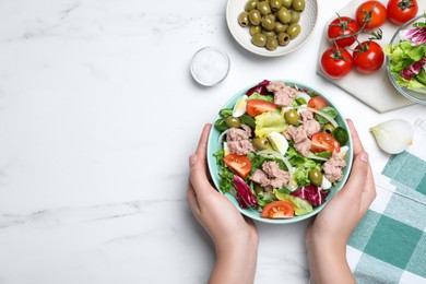 Photo of Woman holding bowl of delicious salad with canned tuna at white table, top view. Space for text