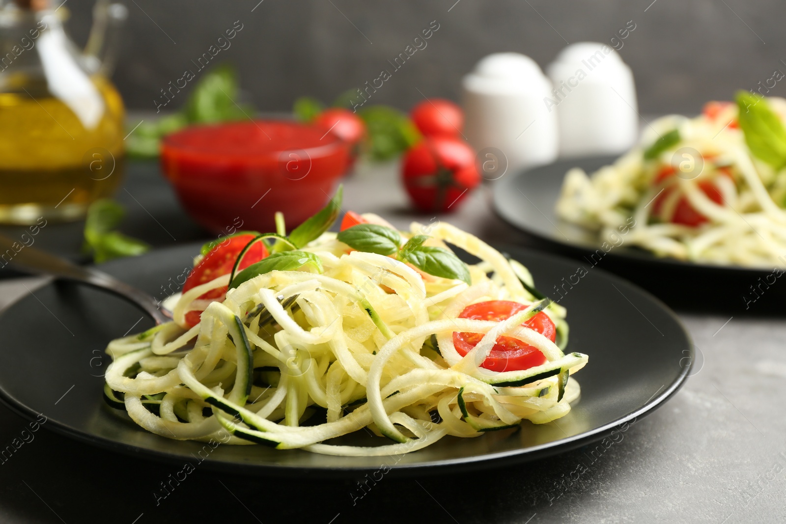 Photo of Delicious zucchini pasta with cherry tomatoes and basil on light grey table, closeup