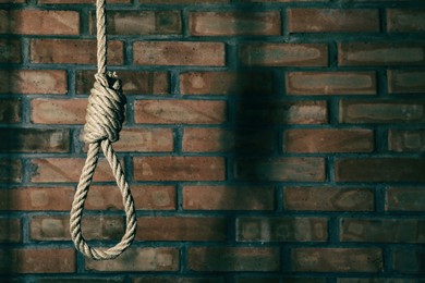 Photo of Rope noose with knot hanging near brick wall, space for text