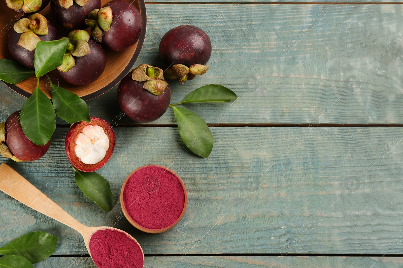 Photo of Purple mangosteen powder and fruits on light blue wooden table, flat lay. Space for text