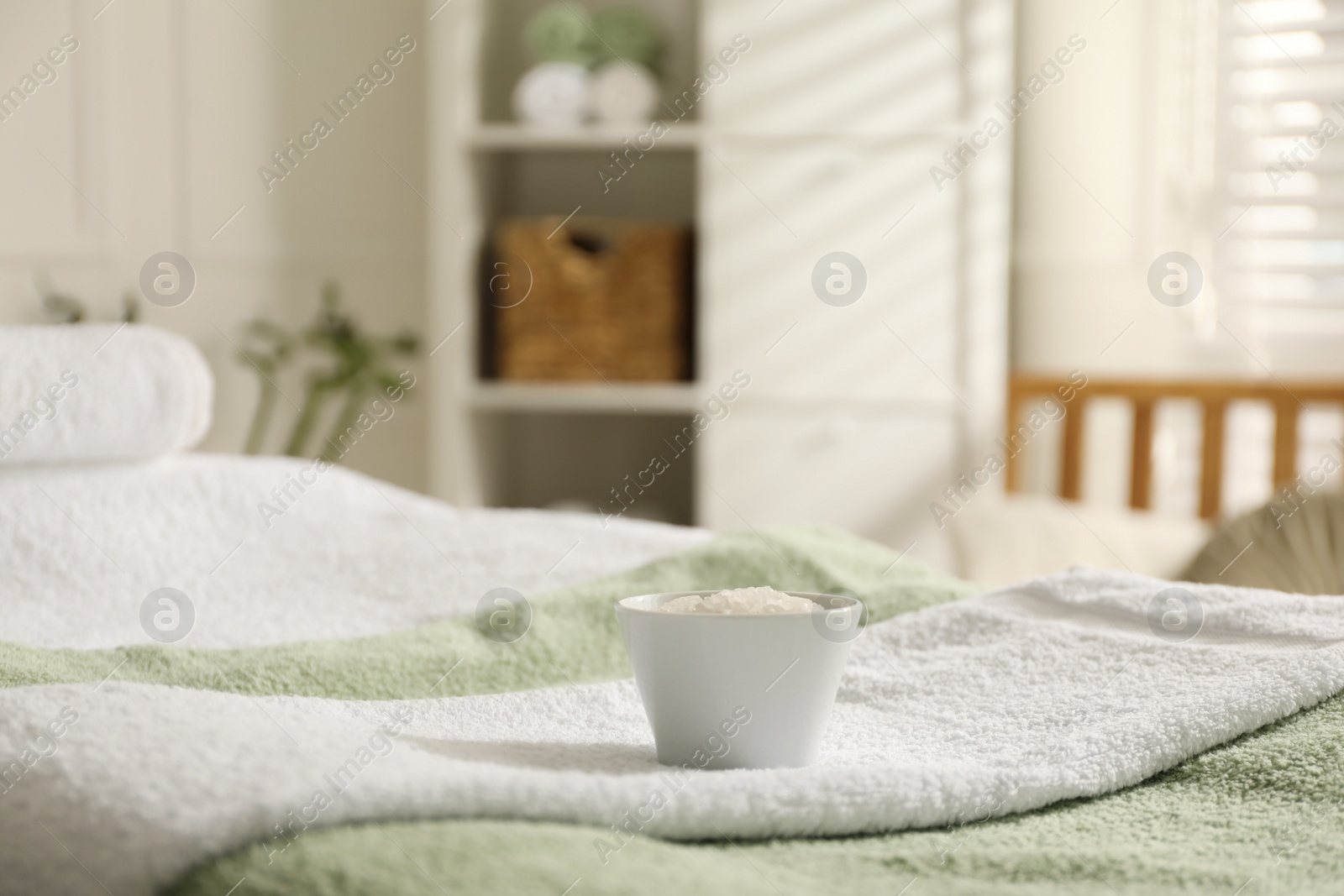 Photo of Soft towels and bowl of sea salt on massage table in spa salon, space for text