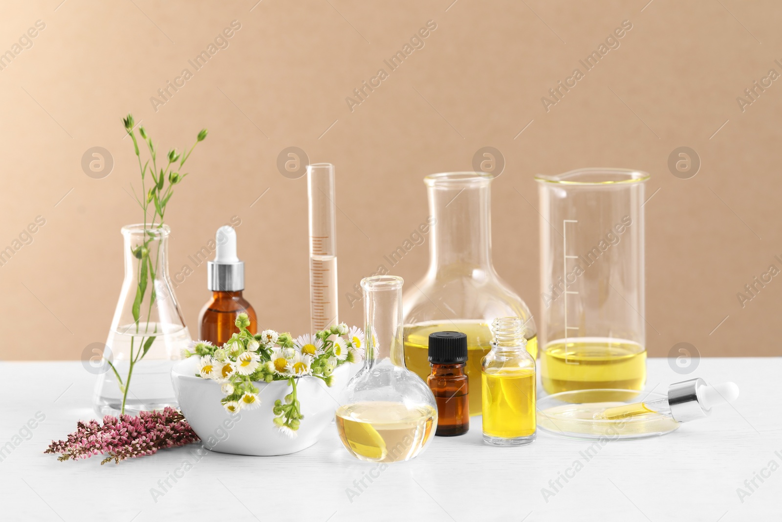 Photo of Developing cosmetic oil. Laboratory glassware and flowers on white table