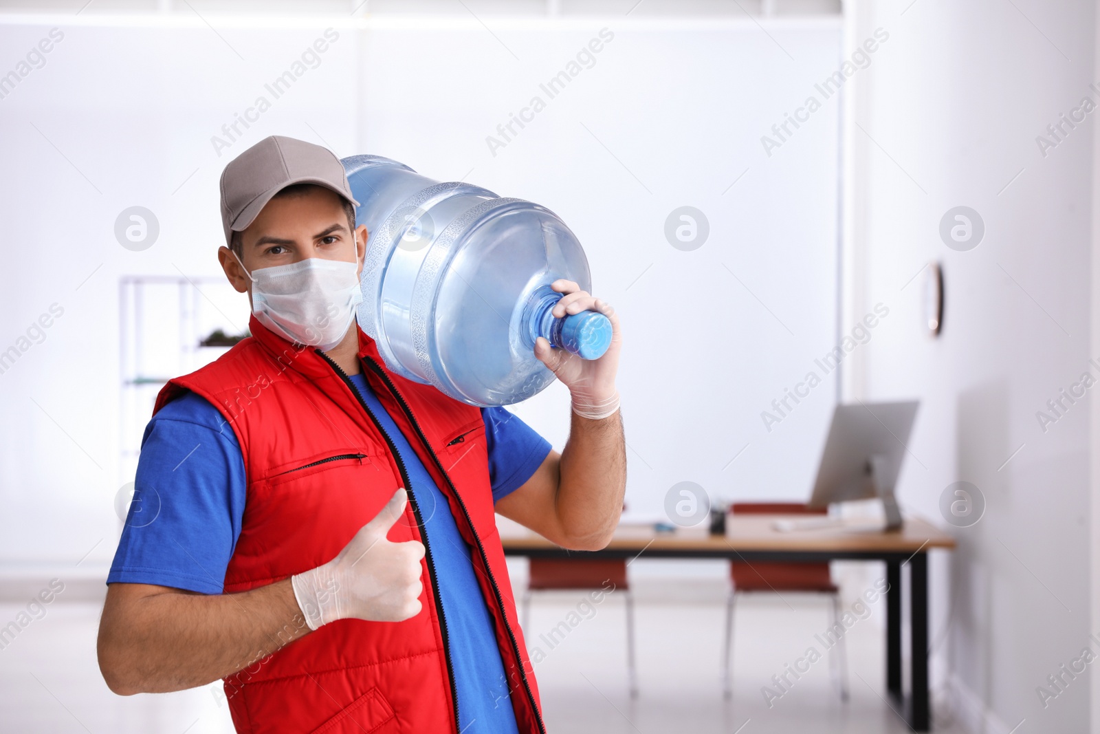 Photo of Courier in mask with bottle of cooler water indoors. Delivery during coronavirus quarantine