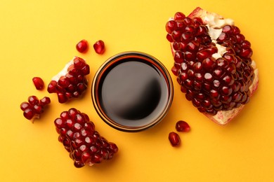 Photo of Glass bowl of tasty pomegranate sauce and fresh ripe fruit on yellow background, flat lay