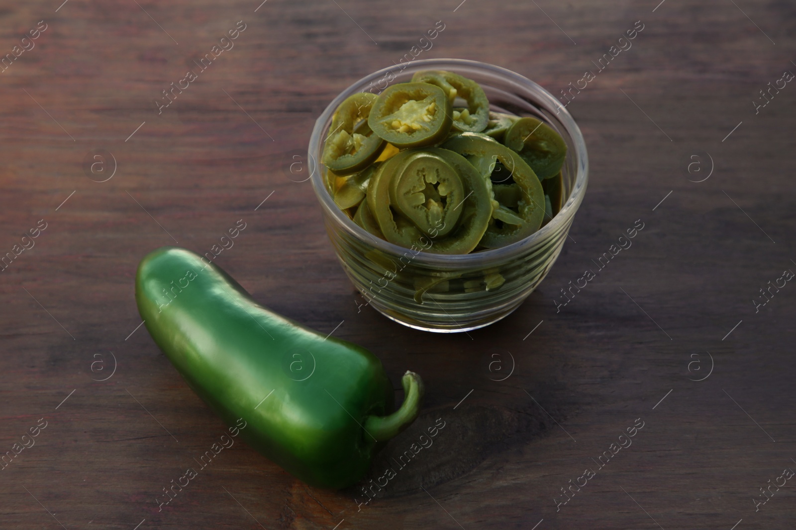 Photo of Fresh and pickled green jalapeno peppers on wooden table