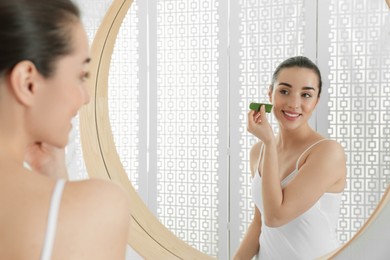 Photo of Young woman with aloe vera leaf near mirror in bathroom