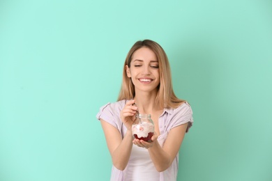 Young attractive woman eating tasty yogurt on color background