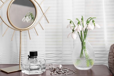 Photo of Beautiful snowdrops in vase, perfume, accessories and mirror on wooden table indoors