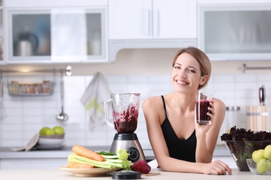 Young woman with glass of tasty healthy smoothie at table in kitchen