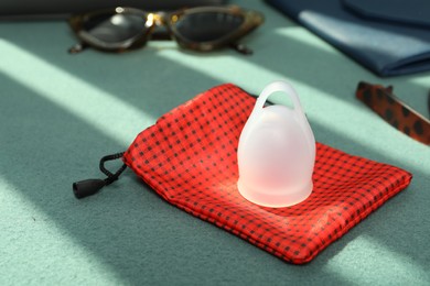 White menstrual cup with red bag on green sofa, space for text
