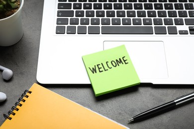 Photo of Paper note with word Welcome, laptop and notebook on grey table, closeup