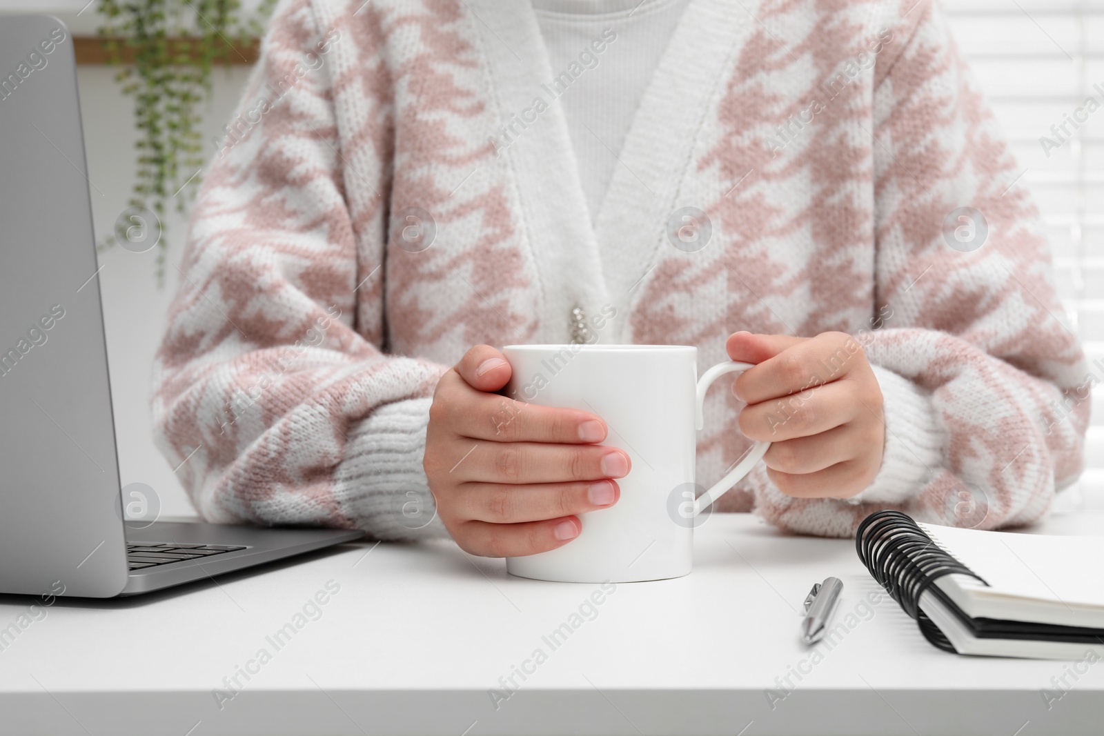 Photo of Woman holding mug at white table, closeup