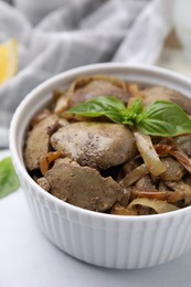 Delicious fried chicken liver with onion and basil in bowl on white table, closeup