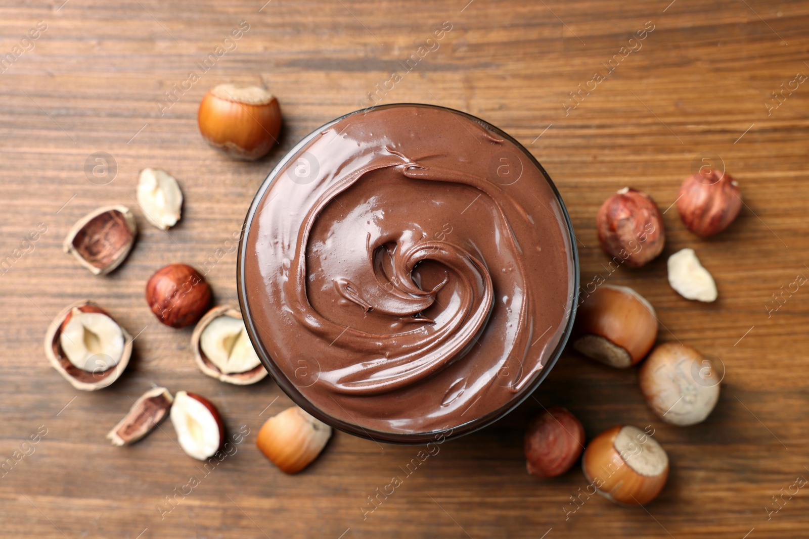 Photo of Tasty chocolate hazelnut spread and nuts on wooden table, flat lay