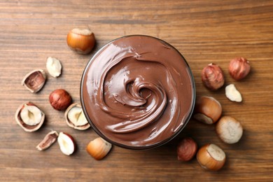 Photo of Tasty chocolate hazelnut spread and nuts on wooden table, flat lay