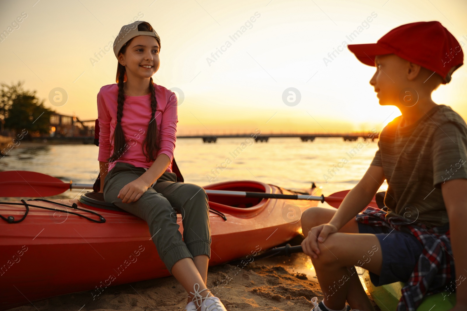 Photo of Happy children sitting on kayaks near river at sunset. Summer camp