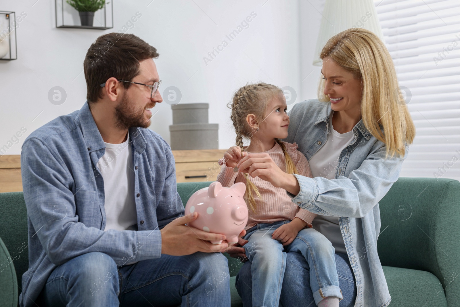 Photo of Planning budget together. Little girl with her parents putting coins into piggybank at home