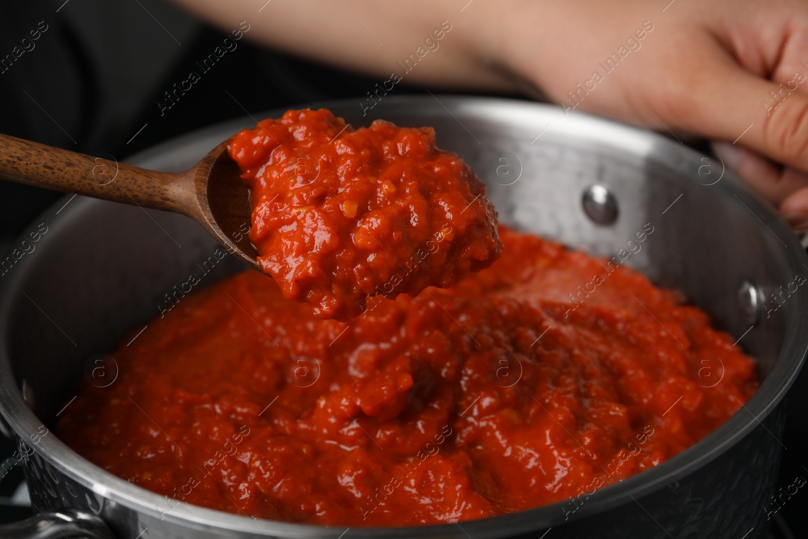 Photo of Woman cooking delicious tomato sauce in pan on stove, closeup