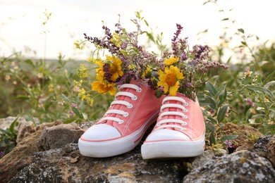 Photo of Shoes with beautiful flowers on stones outdoors