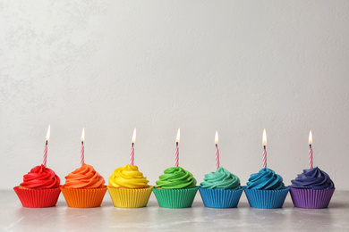 Photo of Delicious birthday cupcakes with burning candles on table