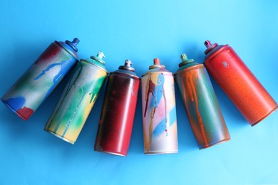 Photo of Many spray paint cans on light blue background, flat lay