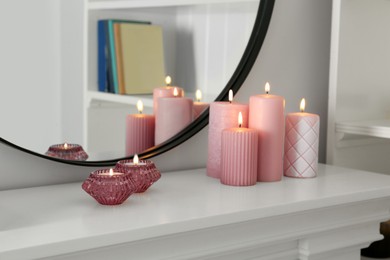 Beautiful burning candles on white console table near mirror indoors