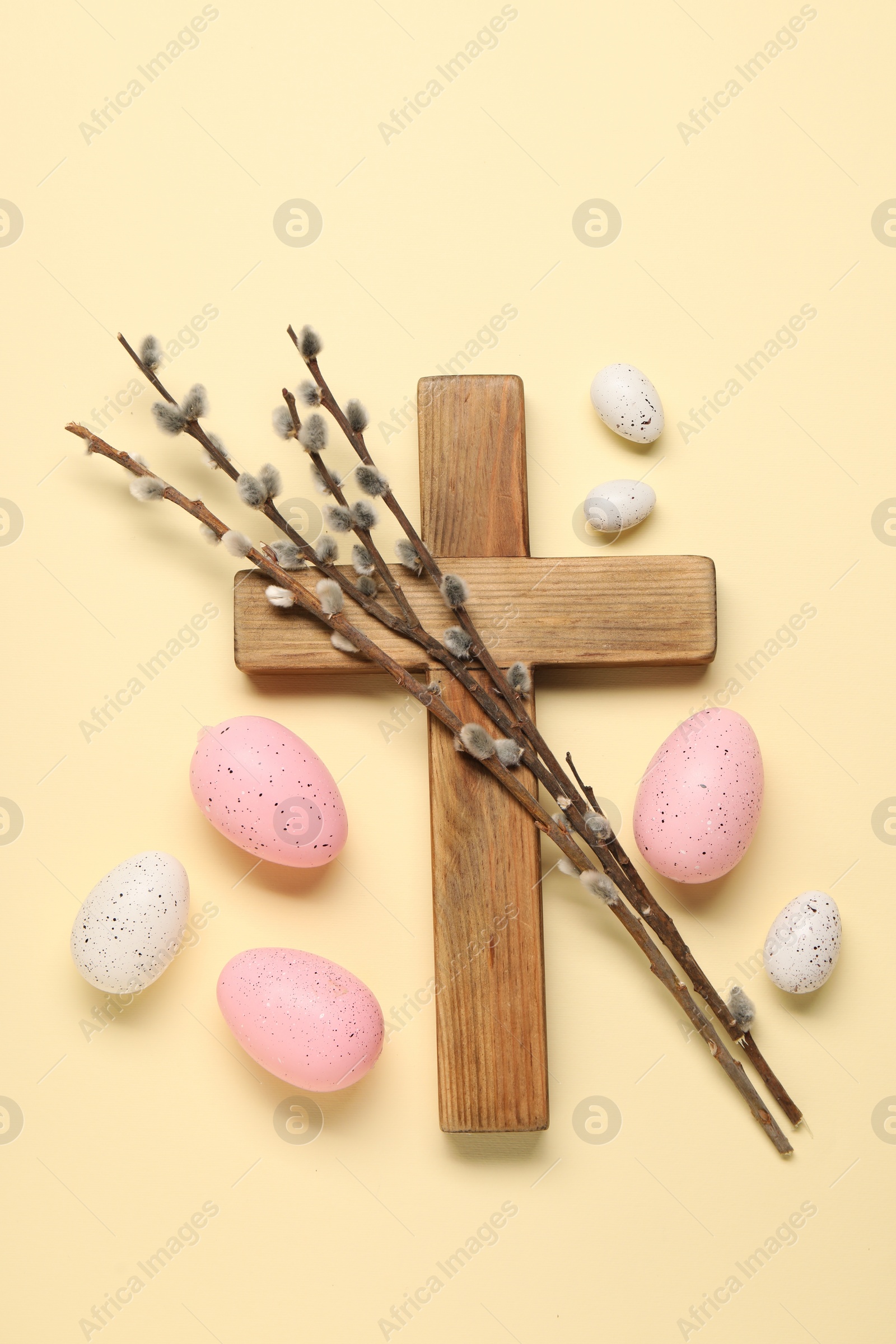 Photo of Wooden cross, painted Easter eggs and willow branches on beige background, flat lay