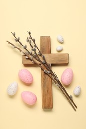 Wooden cross, painted Easter eggs and willow branches on beige background, flat lay