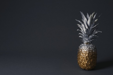 Photo of Pineapple painted with silver and gold on dark background. Space for text