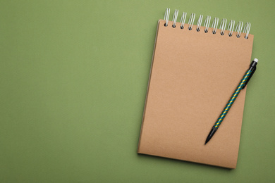 Kraft notebook and pencil on green background, top view. Space for text