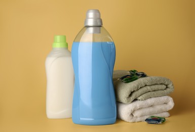 Photo of Bottles of fabric softener, laundry detergent capsules and stacked clean towels on pale yellow background