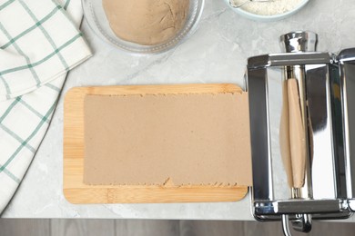 Preparing dough for soba (buckwheat noodles) with pasta maker at light grey table, flat lay