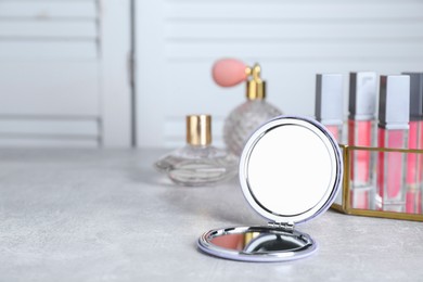 Stylish pocket mirror and cosmetic products on grey table, space for text